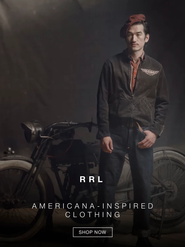 A person wearing a black jacket with a winged logo stands against a dark background next to a vintage motorcycle frame. Text reads “RRL” and “AMERICANA-INSPIRED CLOTHING.” A button says “SHOP NOW.”. 